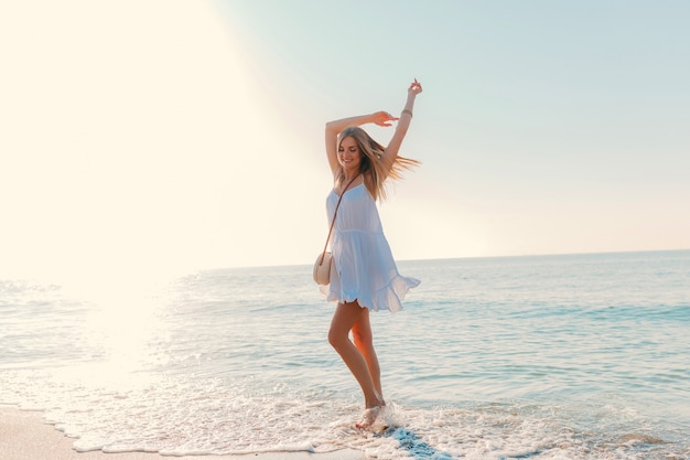 Junge attraktive glückliche Frau, die sich am sonnigen Sommermode-Stil des Seestrandes im Urlaub des weißen Kleides umdreht