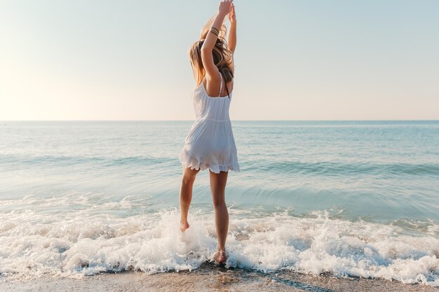 Junge attraktive glückliche Frau, die sich am sonnigen Sommermode-Stil des Seestrandes im Urlaub des weißen Kleides umdreht