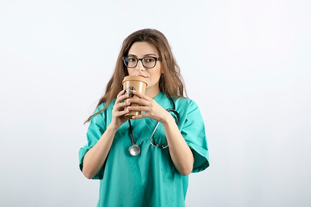 Junge attraktive Krankenschwester mit Stethoskop, die aus einer Tasse Kaffee trinkt