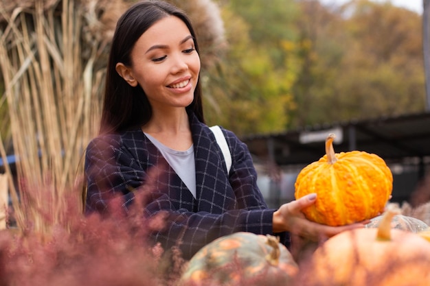 Junge attraktive lässige Frau, die freudig Kürbis für den Halloween-Tag im Herbst-Hofladen im Freien kauft