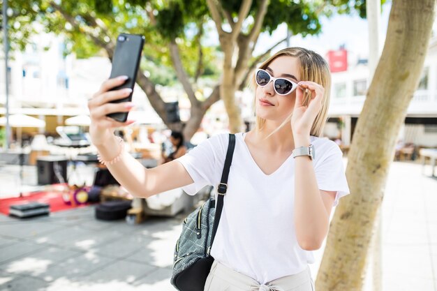 Junge attraktive verspielte Touristenfrau macht Selfie am Telefon draußen