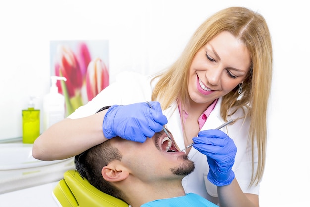 Junge attraktive Zahnärztin, die einen männlichen Patienten in ihrem Büro behandelt