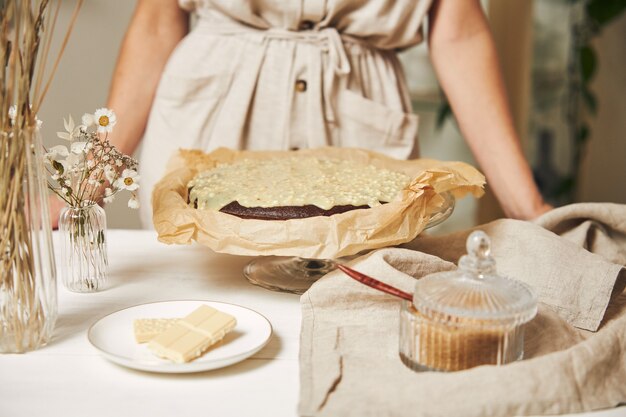 Junge Bäckerin, die einen köstlichen Schokoladenkuchen mit Sahne auf einem weißen Tisch macht