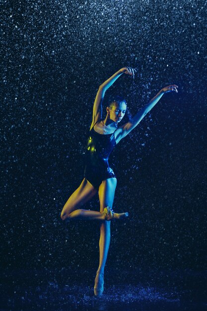 Junge Balletttänzerin, die unter Wassertropfen und -spray durchführt. Kaukasisches Modell, das in Neonlichtern tanzt. Attraktive Frau. Ballett und zeitgenössisches Choreografiekonzept. Kreatives Kunstfoto.