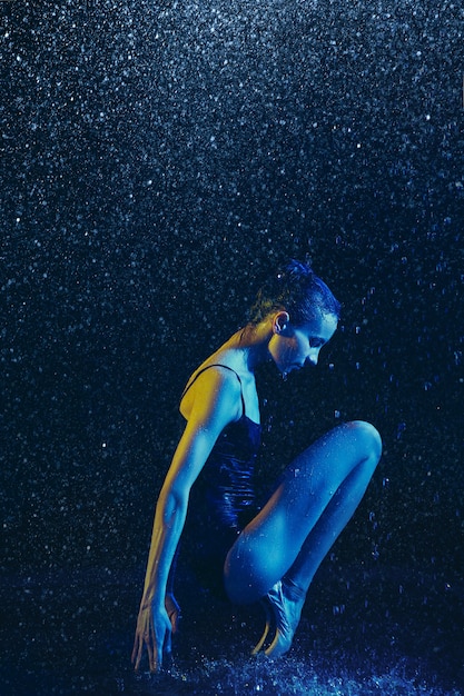 Junge Balletttänzerin, die unter Wassertropfen und -spray durchführt. Kaukasisches Modell, das in Neonlichtern tanzt. Attraktive Frau. Ballett und zeitgenössisches Choreografiekonzept. Kreatives Kunstfoto.
