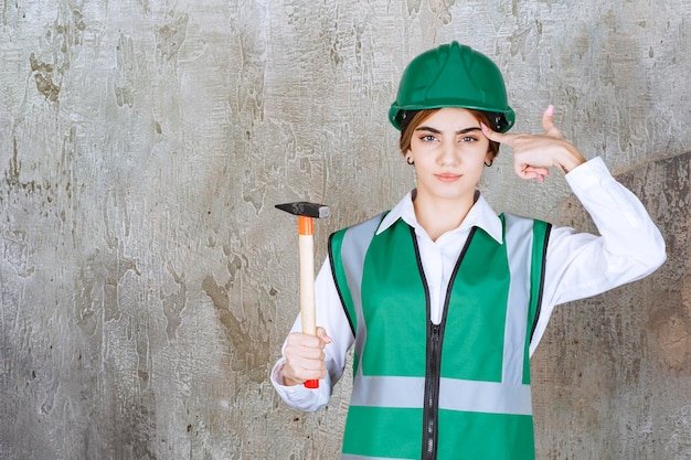 Kostenloses Foto junge bauarbeiterin im grünen helm posiert mit hammer. foto in hoher qualität