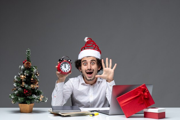 Junge besorgte überraschte Geschäftsperson mit Weihnachtsmannhut und hält Uhr und zeigt fünf im Büro auf dunklem Hintergrund