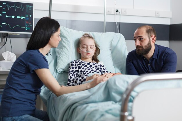 Junge besorgte, unruhige Eltern diskutieren über die Entwicklung der Krankheit kleiner Töchter, während sie sich in der Patientenaufwachstation der Kinderklinik befinden. Ängstlich gestresstes Paar, das über medizinische Behandlung spricht.