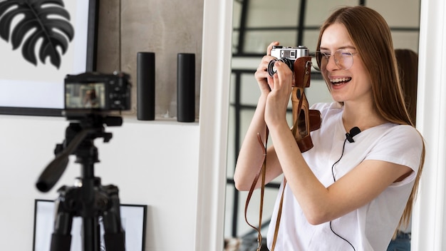 Junge Bloggeraufzeichnung mit professioneller Kamera, die eine Retro-Kamera hält