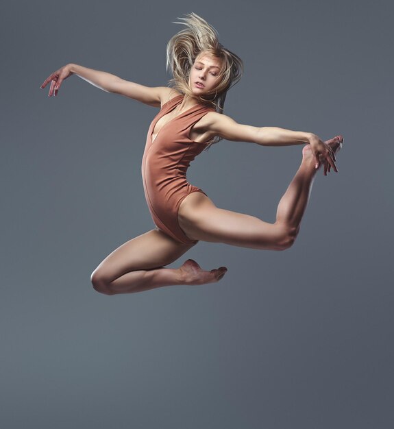 Junge blonde anmutige Ballerina tanzt und springt in einem Studio. Isoliert auf grauem Hintergrund.