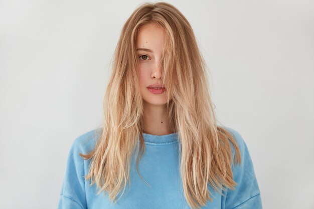 Junge blonde Frau, die blauen Pullover trägt