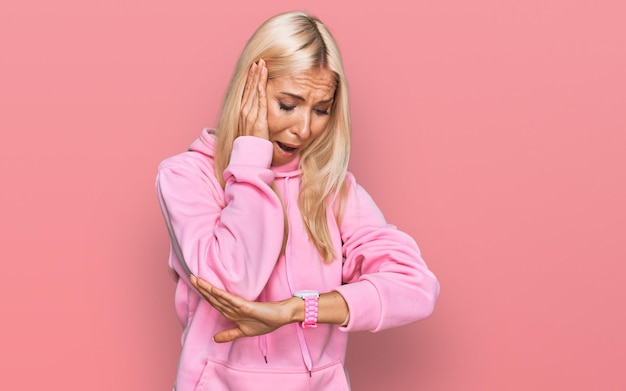 Kostenloses Foto junge blonde frau, die ein lässiges sweatshirt trägt und besorgt auf die uhr schaut, hat angst, zu spät zu kommen