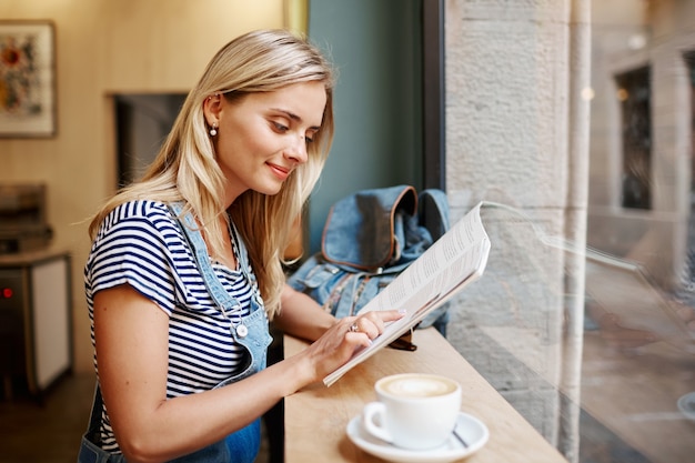 Junge blonde Frau, die im Café sitzt und liest