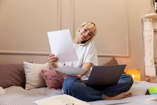 Junge blonde Frau, die von zu Hause aus in ihrem Bett arbeitet