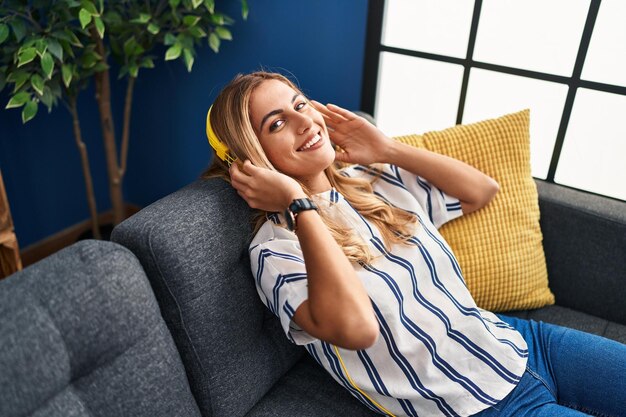 Junge blonde Frau, die zu Hause Musik entspannt auf dem Sofa hört