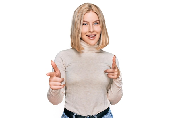 Junge blonde Frau in lässiger Kleidung, die mit fröhlichem und lustigem Gesicht mit dem Finger auf die Kamera zeigt. gute Energie und Stimmung.