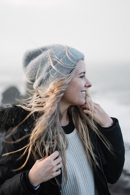 Junge blonde Frau mit einem Hut, der Spaß am Strand bei windigem Wetter hat