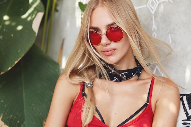 Kostenloses Foto junge blonde frau mit einer roten stilvollen sonnenbrille, wirft innen auf