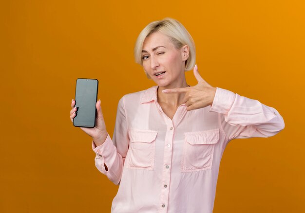 junge blonde slawische Frau hält und zeigt auf Telefon