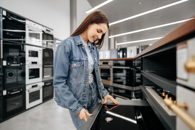 Junge brünette Frau, die einen neuen Elektroherd in einem SB-Warenhaus wählt