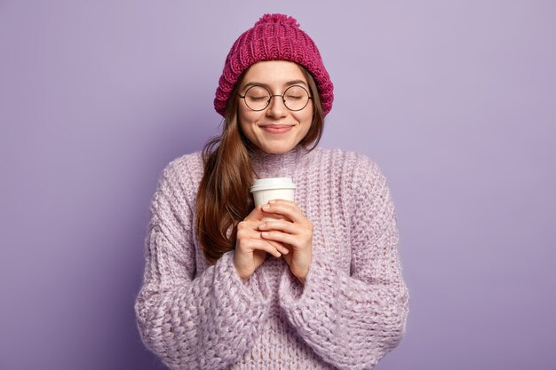 Junge brünette Frau, die lila Pullover trägt und Tasse Kaffee hält