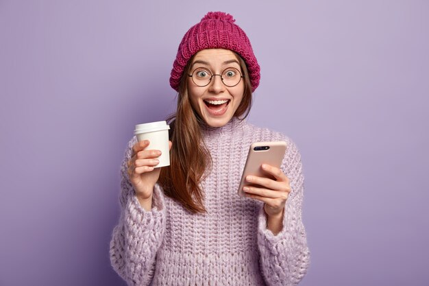 Junge brünette Frau, die lila Pullover trägt und Tasse Kaffee hält