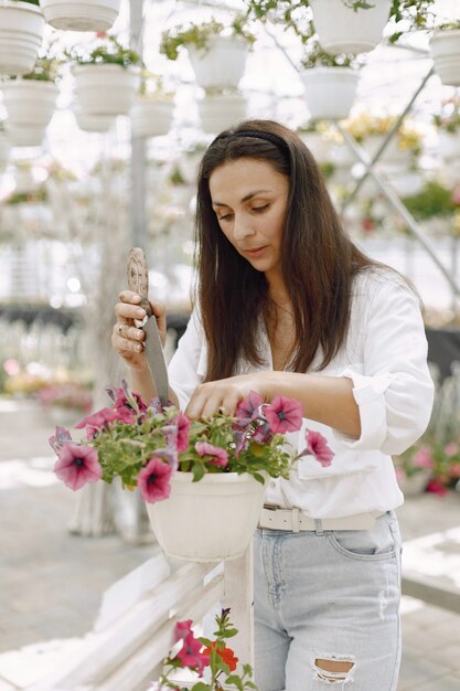 Junge brünette Frau kümmert sich um Topfpflanzen in der Gartenhose. Frau mit weißer Bluse