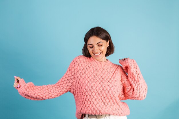 Junge Brünette im warmen rosa Pullover lokalisiert auf blauer Wand