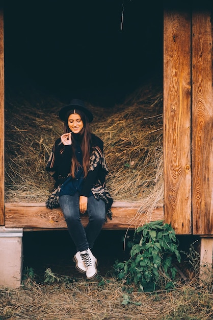 Kostenloses Foto junge brunettefrau, die an der scheune im landhausstil sitzt
