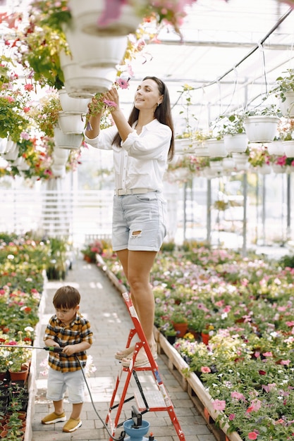 Junge Brunettefrau, die einen Topf mit Anlage in der Gartenhose hängt. Frau mit weißer Bluse