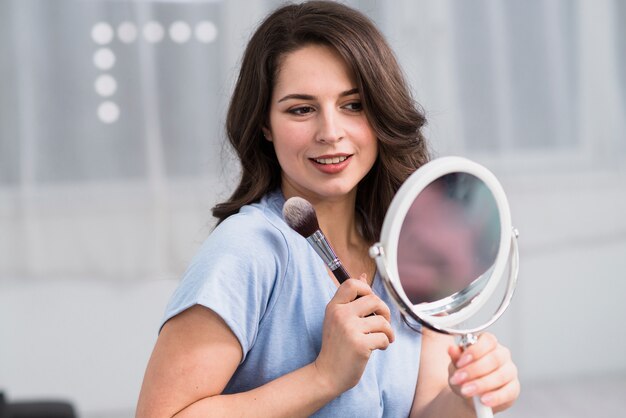 Junge Brunettefrau mit Bürste und rundem Spiegel