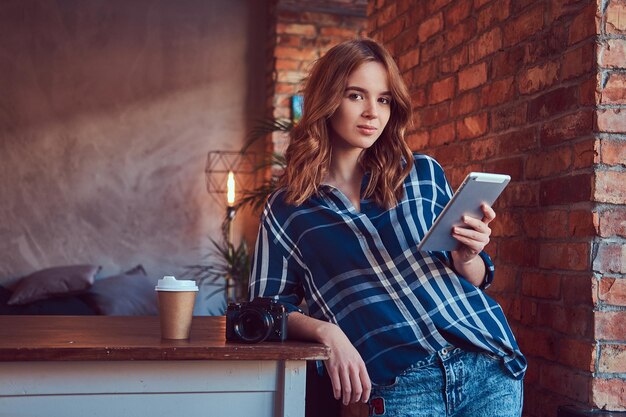 Junge charmante Fotografin, die mit einem Tablet in einem Studio mit Loft-Interieur arbeitet.