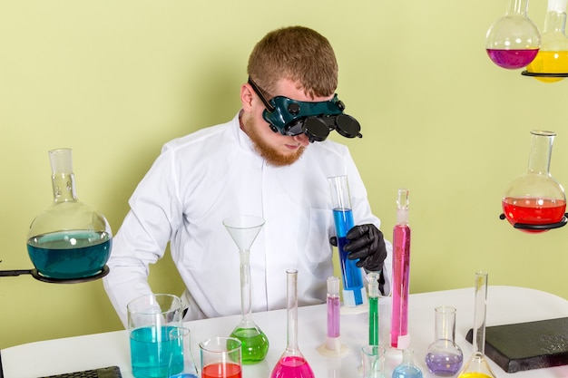 Junge Chemikerin der Vorderansicht, die Schutzbrille zum Betrachten der blauen Chemikalie verwendet