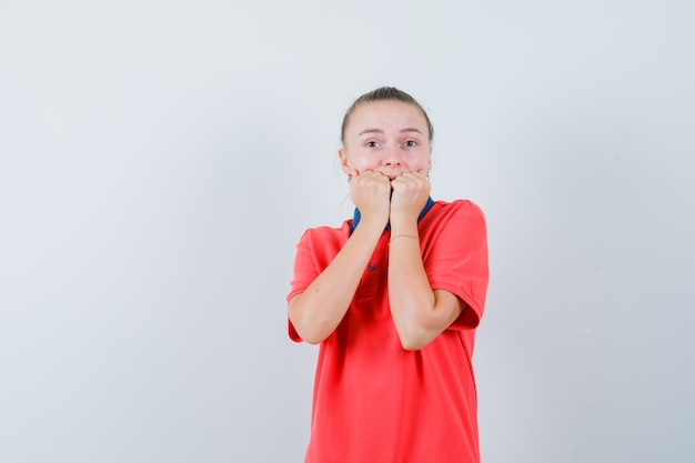 Junge Dame beißt Fäuste emotional im T-Shirt und schaut ängstlich, Vorderansicht.