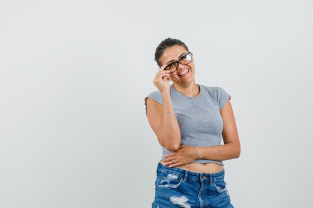 Junge Dame berührt ihre Brille in T-Shirt, Shorts und sieht fröhlich aus.