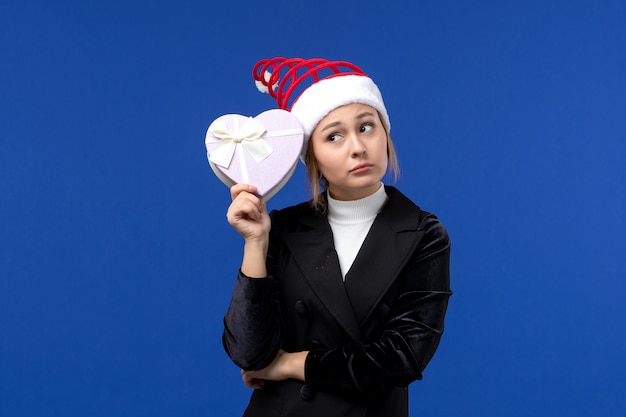 Junge Dame der Vorderansicht, die herzförmiges Geschenk an den Neujahrs-Weihnachtsgeschenken der blauen Wand hält