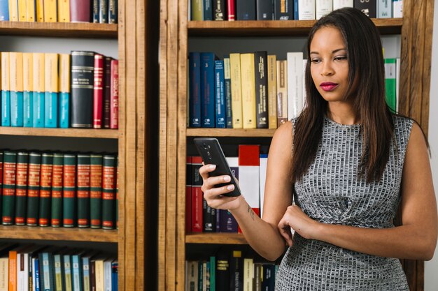 Junge Dame des Afroamerikaners, der Smartphone nahe Büchern verwendet