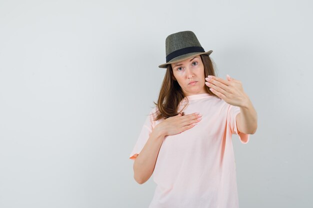 Junge Dame, die Ablehnungsgeste im rosa T-Shirt Hut zeigt und entschlossen schaut