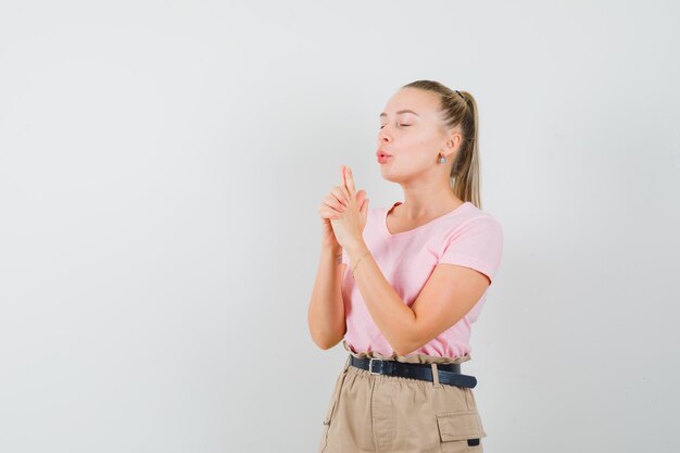 Junge Dame, die auf Fingerpistole im T-Shirt, in der Hose bläst und selbstbewusst aussieht. Vorderansicht.