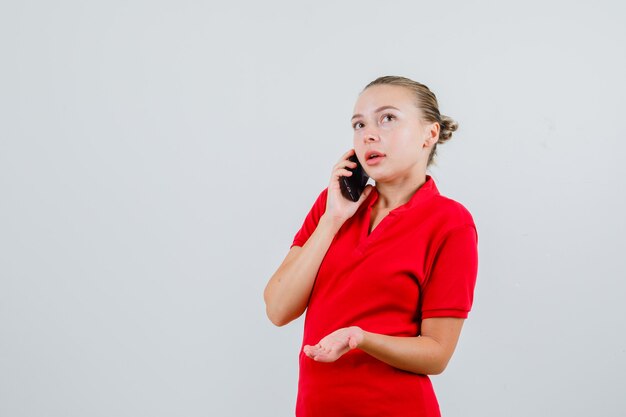 Junge Dame, die auf Handy in rotem T-Shirt spricht und nachdenklich schaut
