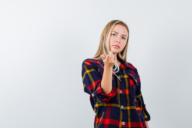 Junge Dame, die auf Kamera im karierten Hemd zeigt und selbstbewusst, Vorderansicht schaut.