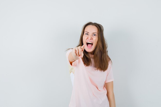 Junge Dame, die auf Kamera zeigt, während sie im rosa T-Shirt schreit und verrückt aussieht