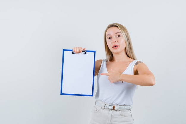 Junge Dame, die auf leere Zwischenablage in weißer Bluse zeigt und konzentriert schaut