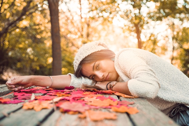 Junge Dame, die auf Tabelle mit Herbstblättern liegt