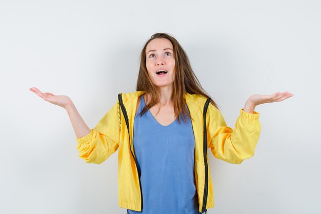 Junge Dame, die ausgebreitete Handflächen anhebt, im T-Shirt aufschaut und hoffnungsvoll aussieht. Vorderansicht.