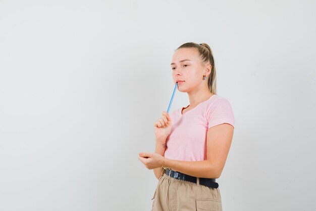 Junge Dame, die Bleistift im T-Shirt und in der Hose hält und nachdenklich aussieht