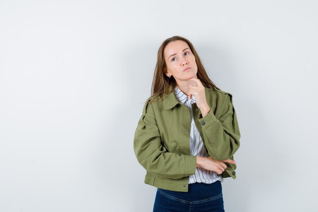 Junge Dame, die das Kinn auf dem Finger in Bluse, Jacke stützt und nachdenklich aussieht, Vorderansicht.