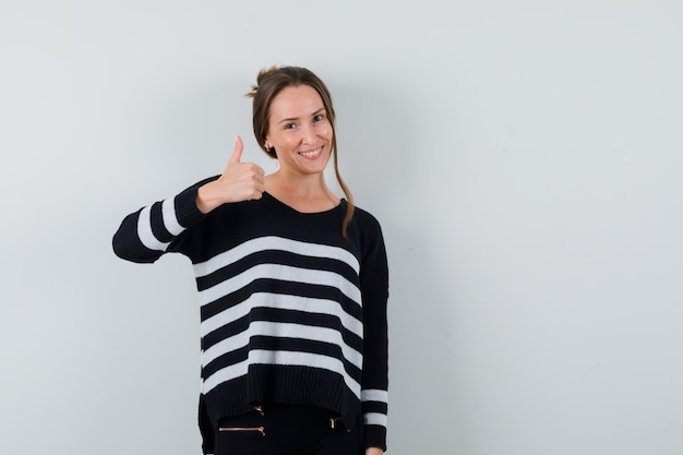 Junge Dame, die Daumen oben im Hemd zeigt und lustig schaut