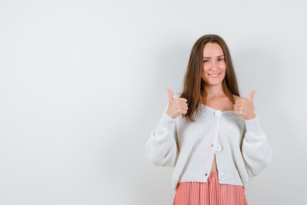 Junge Dame, die Daumen oben in Strickjacke und Rock zeigt, die glücklich lokalisiert aussehen