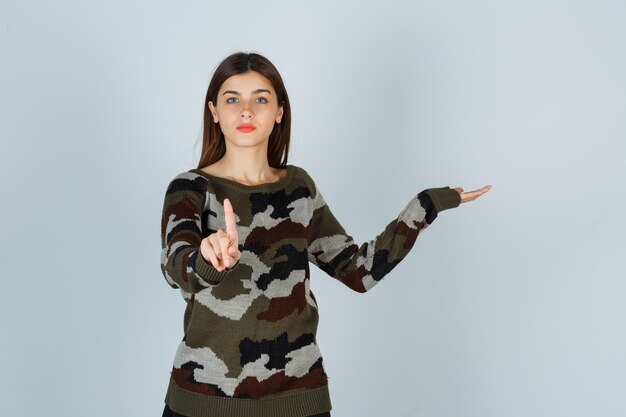 Junge Dame, die eine winzige Geste zeigt, während sie vorgibt, etwas im Pullover zu zeigen